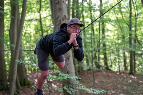 Person balanciert auf einer gespannten Schnur zwischen Bäumen im Wald