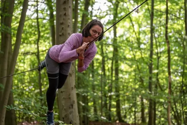 Person balanciert auf einer gespannten Seilbrücke zwischen Bäumen