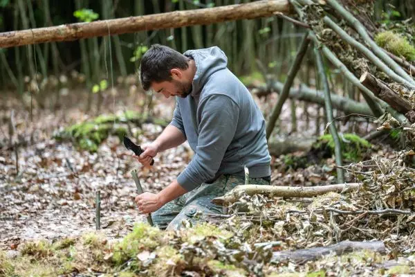 Person bearbeitet einen Stock mit einem Messer im Wald
