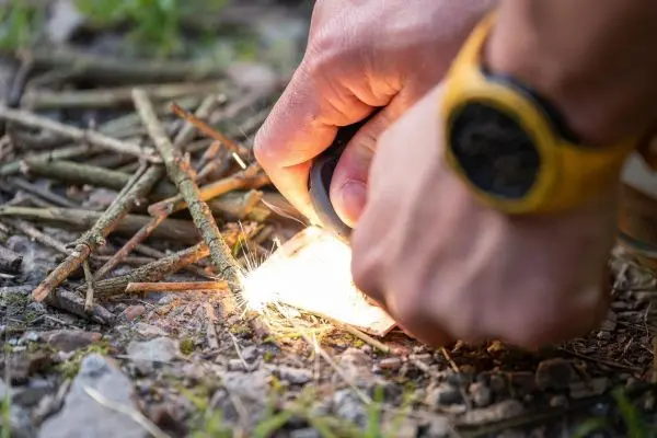 Person erzeugt Funken mit Feuerstahl auf trockenem Holz