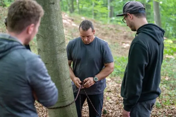 Person knotet ein Seil um einen Baum, während andere zuschauen