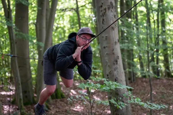 Person nutzt selbstgebaute Seilbrücke zwischen Bäumen im Wald