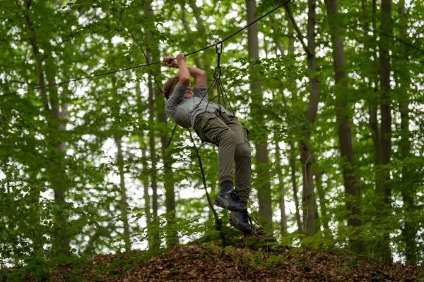 Person schwingt an einer Seilbrücke zwischen Bäumen im Wald