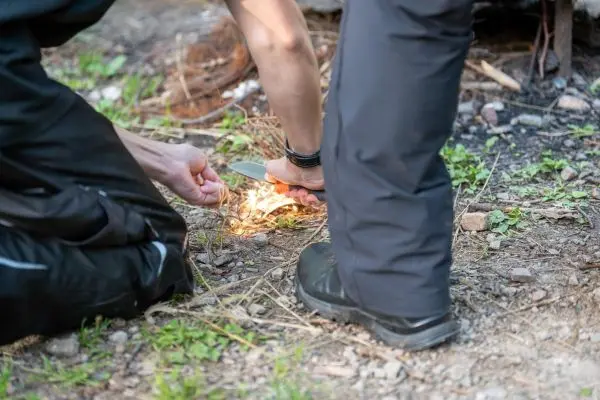 Person zündet mit einem Messer trockenes Gras an