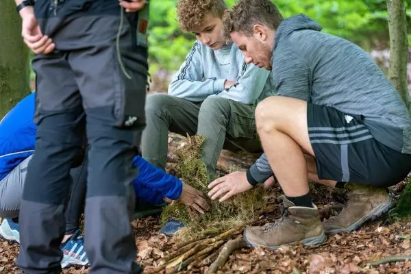 Personen sammeln Materialien für ein Feuer im Wald beim Survival Training