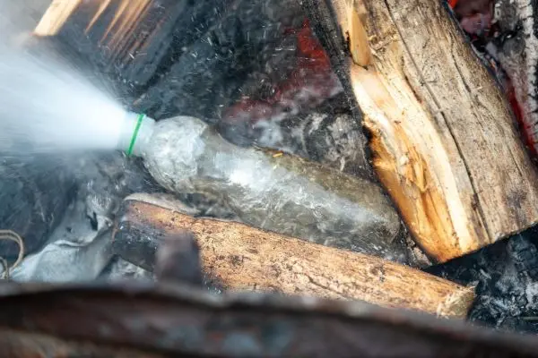 Wasserflasche spritzt in einem Feuer mit Holzscheiten beim Überlebenstraining