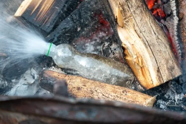 Wasserflasche sprüht Wasser auf brennendes Holz im Feuer