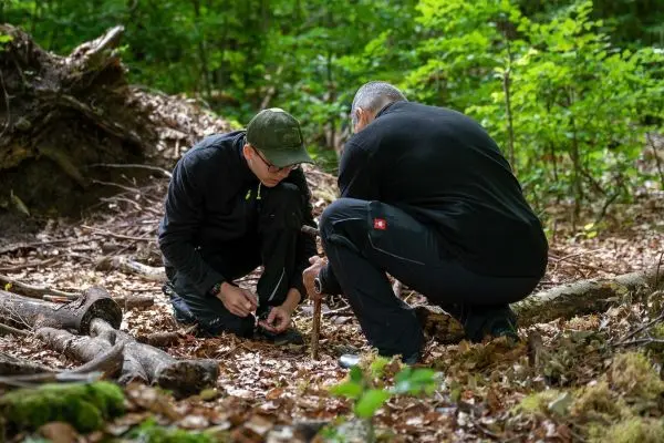 Zwei Personen knien im Wald und bereiten eine Holzstruktur vor