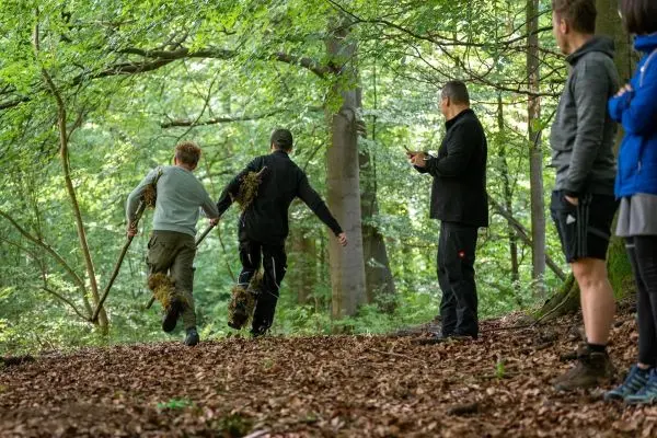 Zwei Personen tragen Laub und rennen durch den Wald, während andere zuschauen
