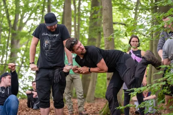 Zwei Personen ziehen an einem Seil in einem Waldgebiet