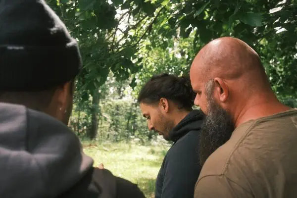 Drei Personen betrachten gemeinsam etwas im Freien unter Bäumen