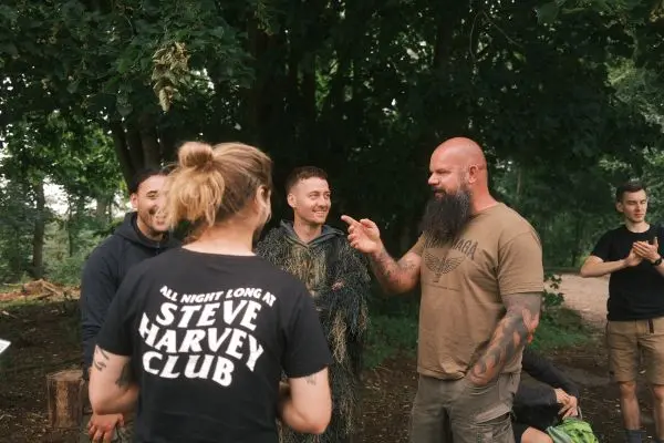 Gruppe diskutiert im Wald, einige tragen Tarnkleidung und lächeln