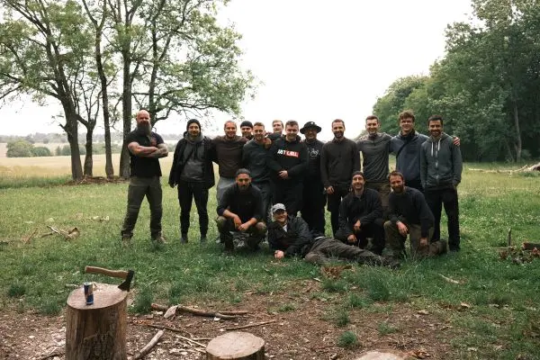 Gruppe von Personen steht auf einer Wiese, umgeben von Bäumen und Holzstämmen