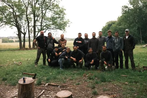 Gruppe von Personen steht auf einer Wiese vor Bäumen und Holzstämmen