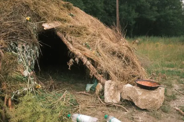 Hütte aus Ästen und Gras mit einem Kochtopf daneben