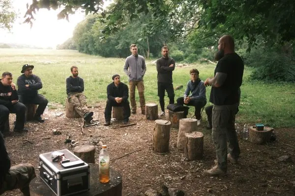 Mann erklärt einer Gruppe auf Baumstümpfen im Freien Survival-Techniken