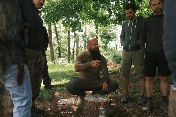 Mann erklärt Techniken im Freien, umgeben von Zuhörern auf einer Lichtung