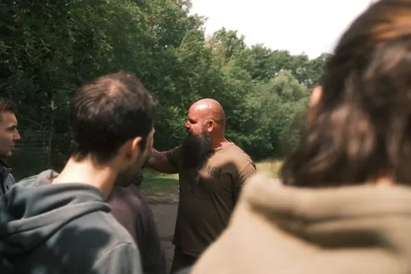 Mann mit Bart erklärt einer Gruppe im Freien eine Technik