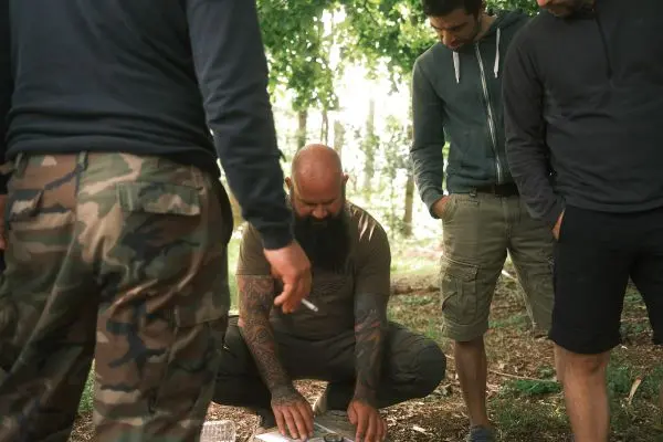 Mann mit Tätowierungen betrachtet eine Karte auf dem Boden, umgeben von anderen