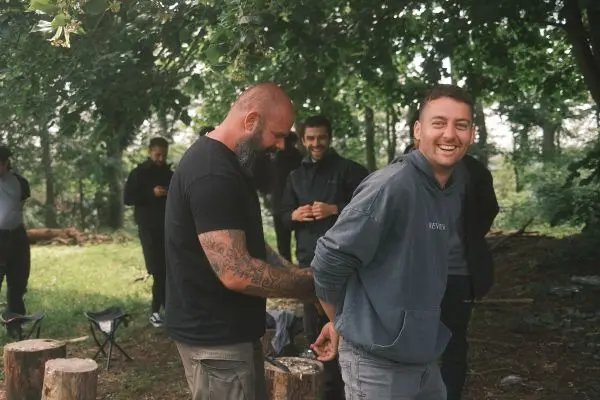 Person bindet Hände einer anderen Person, weitere Personen im Hintergrund