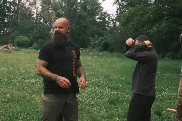 Zwei Männer stehen auf einer Wiese, einer zieht sich ein Oberteil über