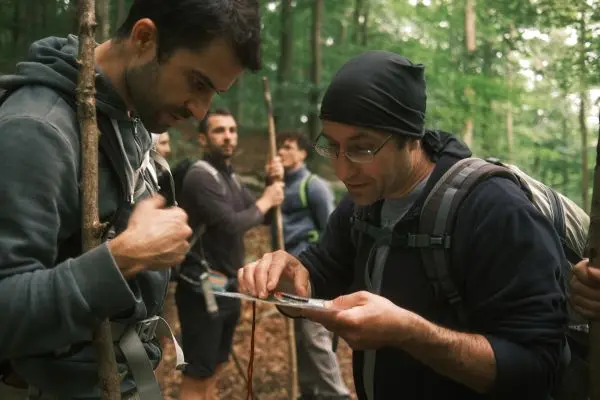 Zwei Personen betrachten ein GPS-Gerät im Wald, während andere im Hintergrund stehen