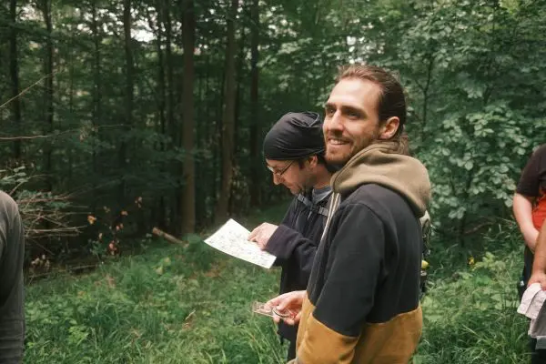 Zwei Personen betrachten eine Karte im Wald, während eine weitere Person im Hintergrund steht