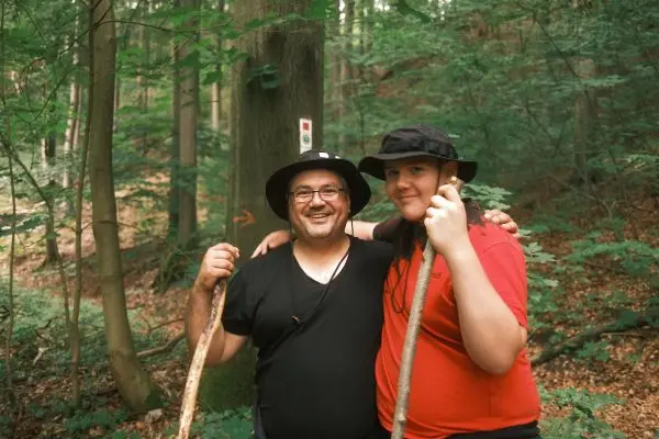 Zwei Personen halten Wanderstöcke in einem Wald mit markierten Bäumen