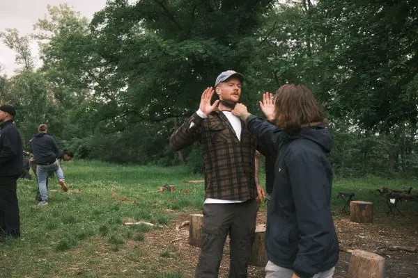 Zwei Personen üben eine Kommunikationsübung im Freien, umgeben von Bäumen