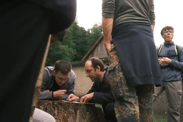 Zwei Personen untersuchen eine Karte auf einem Baumstamm, während andere zuschauen