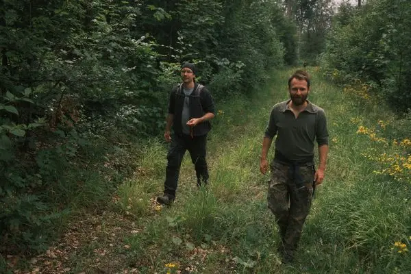 Zwei Personen wandern auf einem schmalen Pfad durch einen bewaldeten Bereich