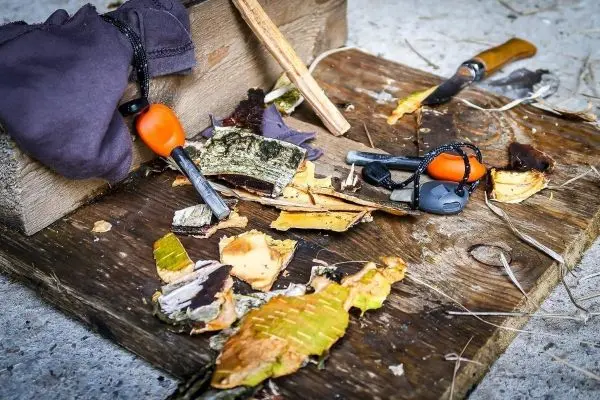 Feuerstahl und Zunder auf Holzunterlage mit Messer und Rinde