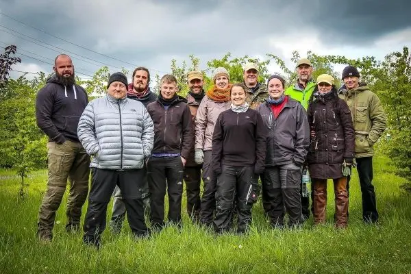 Gruppierung von Personen in Outdoor-Bekleidung auf einer Wiese mit Bäumen im Hintergrund
