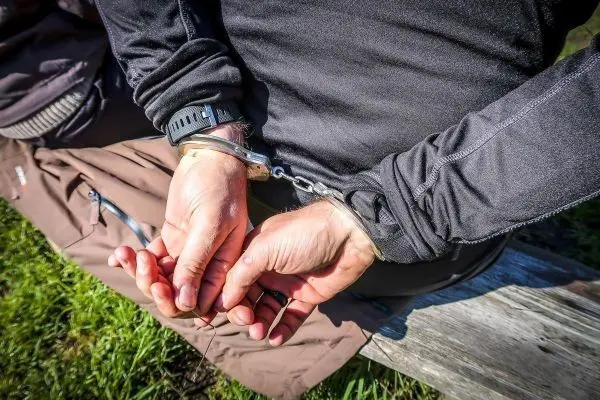 Hände mit Handschellen hinter dem Rücken auf einer Holzbank
