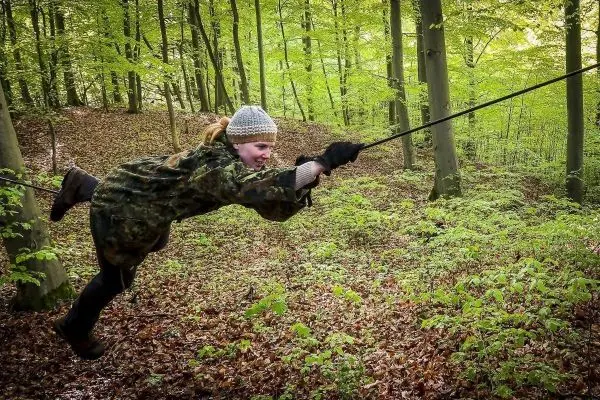 Kind schwingt an selbstgebauter Seilbrücke zwischen Bäumen im Wald