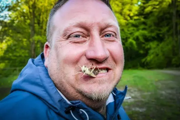 Mann mit Heuschrecke auf der Lippe lächelt in die Kamera