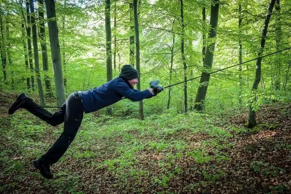 Person nutzt Seil für eine selbstgebaute Seilbrücke im Wald