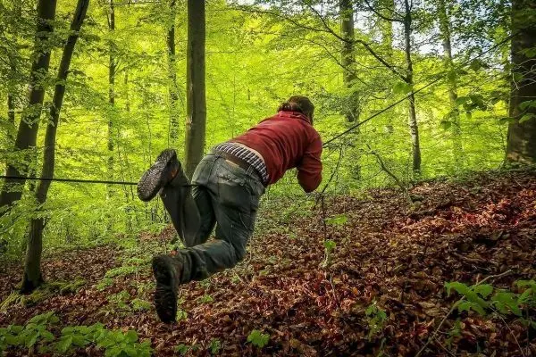 Person nutzt Seil zur Fortbewegung über einen Hang im Wald