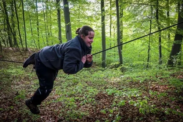 Person schwingt an einem Seil zwischen Bäumen im Wald