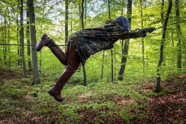 Person schwingt an einer Seilbrücke zwischen Bäumen im Wald
