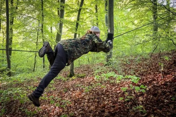 Person schwingt sich an einer Seilbrücke durch den Wald