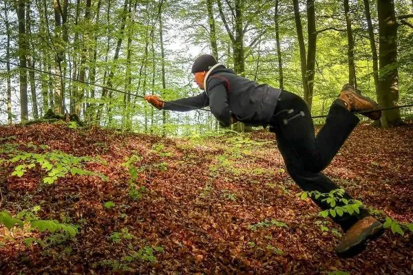 Person zieht sich an einem Seil über den Waldboden