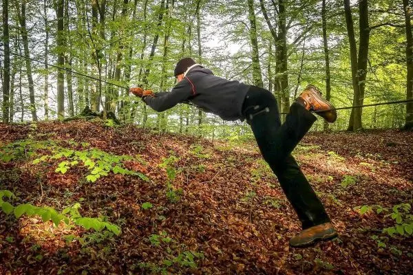 Person zieht sich an einem Seil über einen mit Laub bedeckten Hang