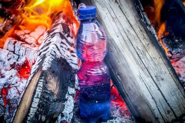 Wasserflasche steht zwischen brennenden Holzscheiten im Feuer