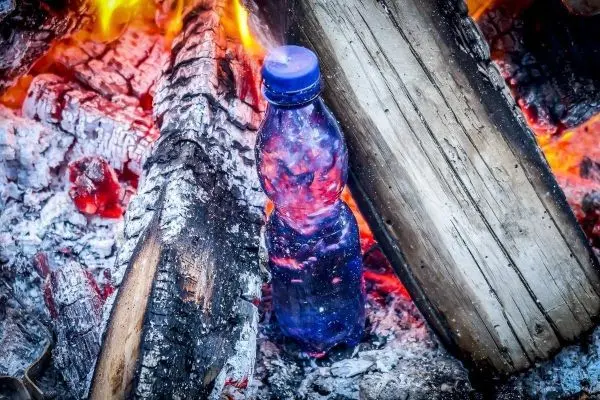 Wasserflasche steht zwischen glühenden Holzscheiten im Feuer