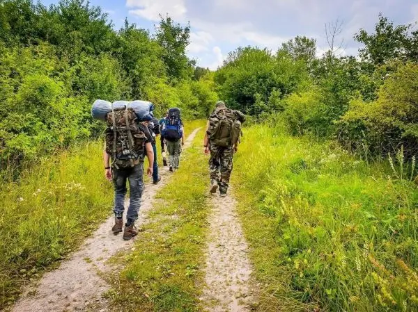 Drei Personen mit Rucksäcken wandern einen schmalen Weg entlang