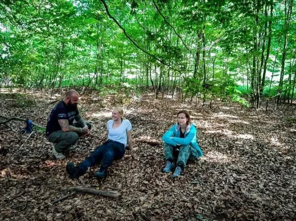 Drei Personen sitzen im Laub unter Bäumen und unterhalten sich