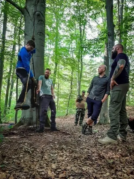Ein Mann schwingt an einem Seil von einem Baum, während andere zuschauen
