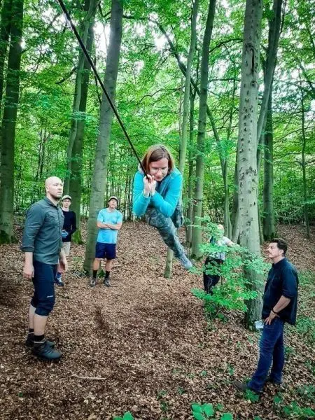 Frau schwingt an Seil über den Waldboden, umgeben von mehreren Beobachtern