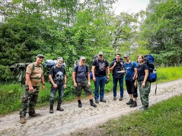 Gruppe mit Rucksäcken steht auf einem Waldweg zwischen Bäumen und Gras